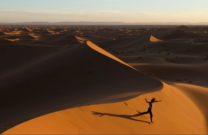 Aerial view of a person running down a large sand dune in the desert under a warm sunset sky captured by Peter Bohler.