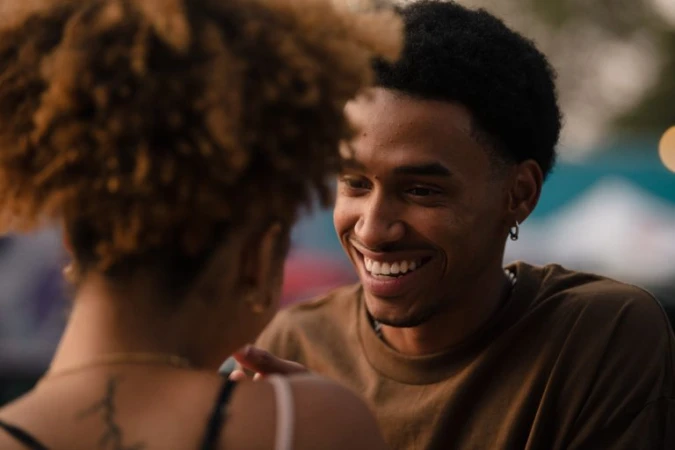 Close-up of a smiling black man looking towards a woman whose back is turned in the foreground, captured by Peter Bohler.