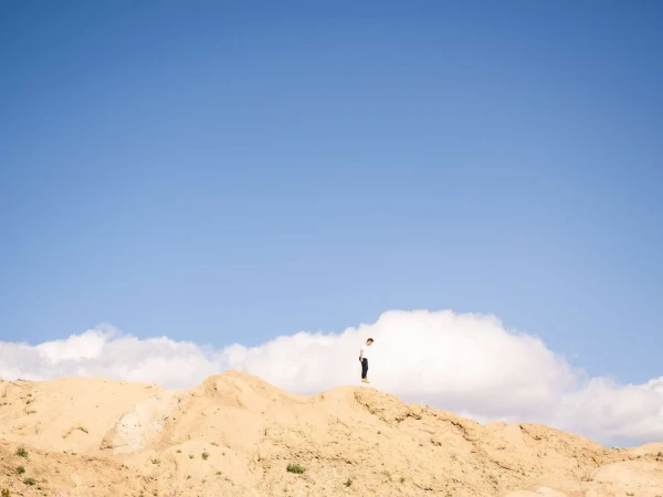 A lone person stands on a sandy hill under a vast blue sky with white clouds, photographed by Peter Bohler.