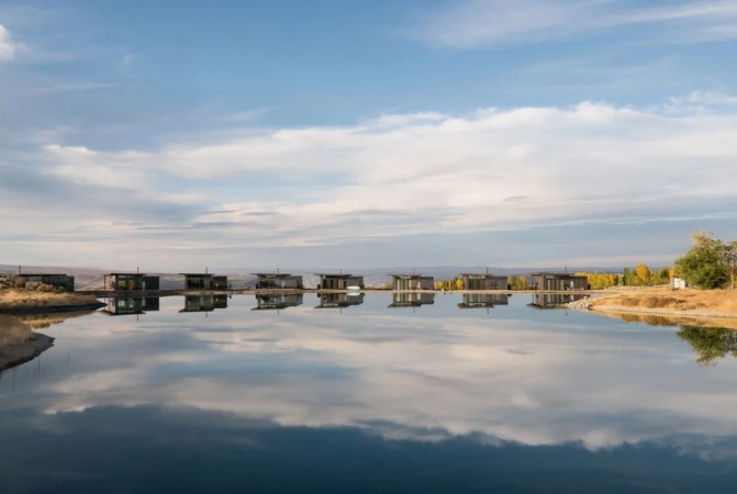 Modern cabins lined up along a calm body of water reflecting the sky and buildings under soft daylight by Peter Bohler