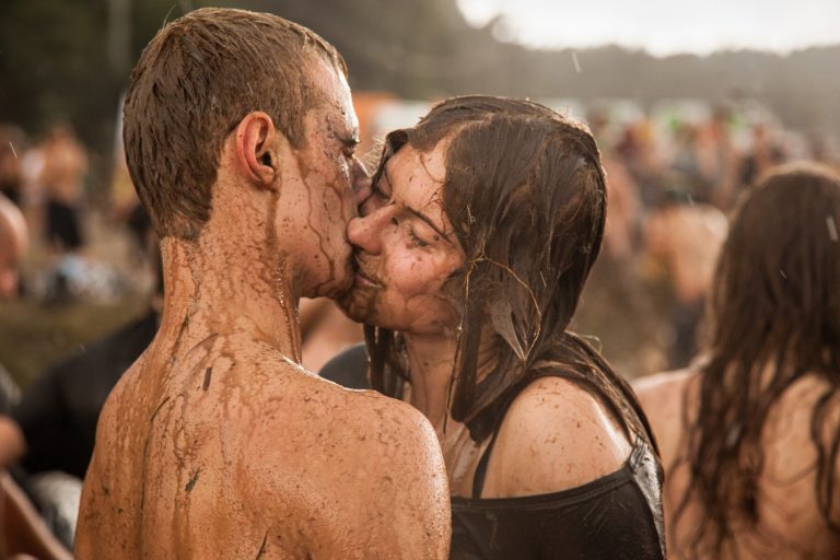 Close-up profile of a couple covered in mud kissing passionately outdoors at a festival event.
