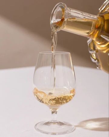 Golden amber liquid being poured from a decanter into a clear stemmed glass on a white tablecloth