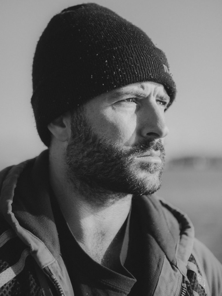 Close-up black and white portrait of a man wearing a beanie and hooded jacket, looking away