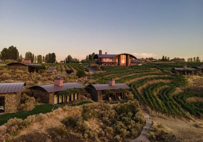 Scenic landscape of stone buildings with vineyard in background. Outdoor setting at sunset, featuring rustic architecture and natural beauty.