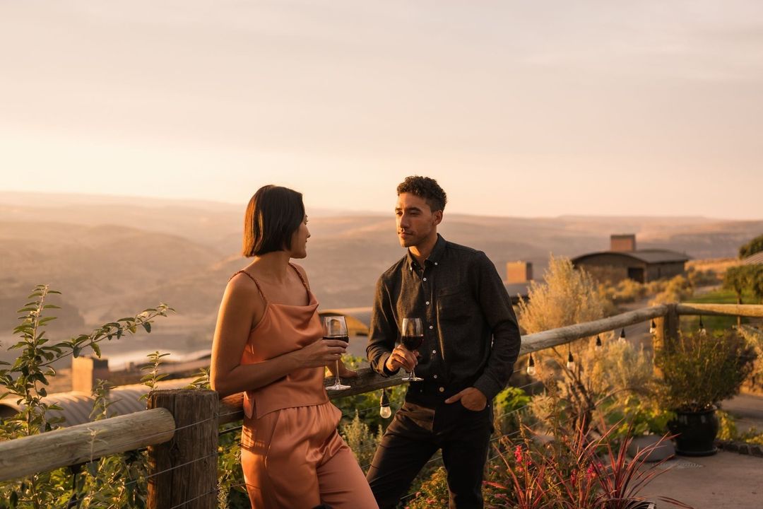 A couple enjoys wine at sunset on a scenic overlook with rolling hills, showcasing relaxation and a shared moment against a beautiful backdrop.