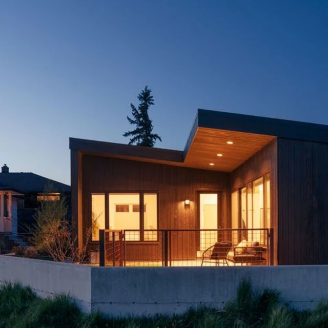 Modern house with wood siding and a patio featuring outdoor seating, set against a twilight sky with landscape, architecture.
