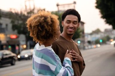 A smiling young Black man and woman interacting outdoors on an urban street at dusk by photographer Peter Bohler.