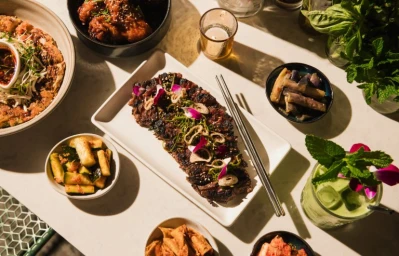 Overhead food photography by Peter Bohler featuring Korean dishes, grilled galbi, side dishes, and a cocktail on a table.