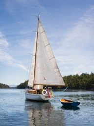 White sailboat with a tall triangular sail anchored in calm water with a small blue dinghy nearby under a clear sky.