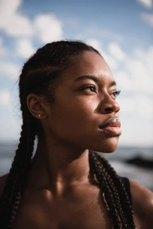 Portrait of a Black woman with braided hair looking away under a cloudy blue sky by photographer Peter Bohler.