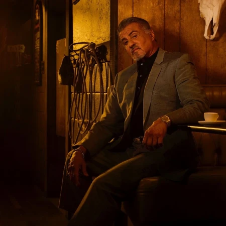 Portrait of an adult male in a suit jacket sitting indoors, with a cup on the table and an animal skull on the wall in the background.