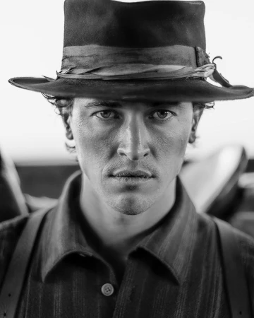 Close-up monochrome portrait of a man wearing a wide-brimmed fedora hat and dark buttoned shirt