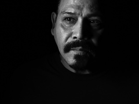 Black and white portrait of an adult male with a mustache and goatee against a dark backdrop in dramatic chiaroscuro lighting.