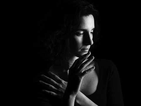 Black and white portrait of a woman with hand near her face and arms crossed, set against a dark background, with chiaroscuro lighting.