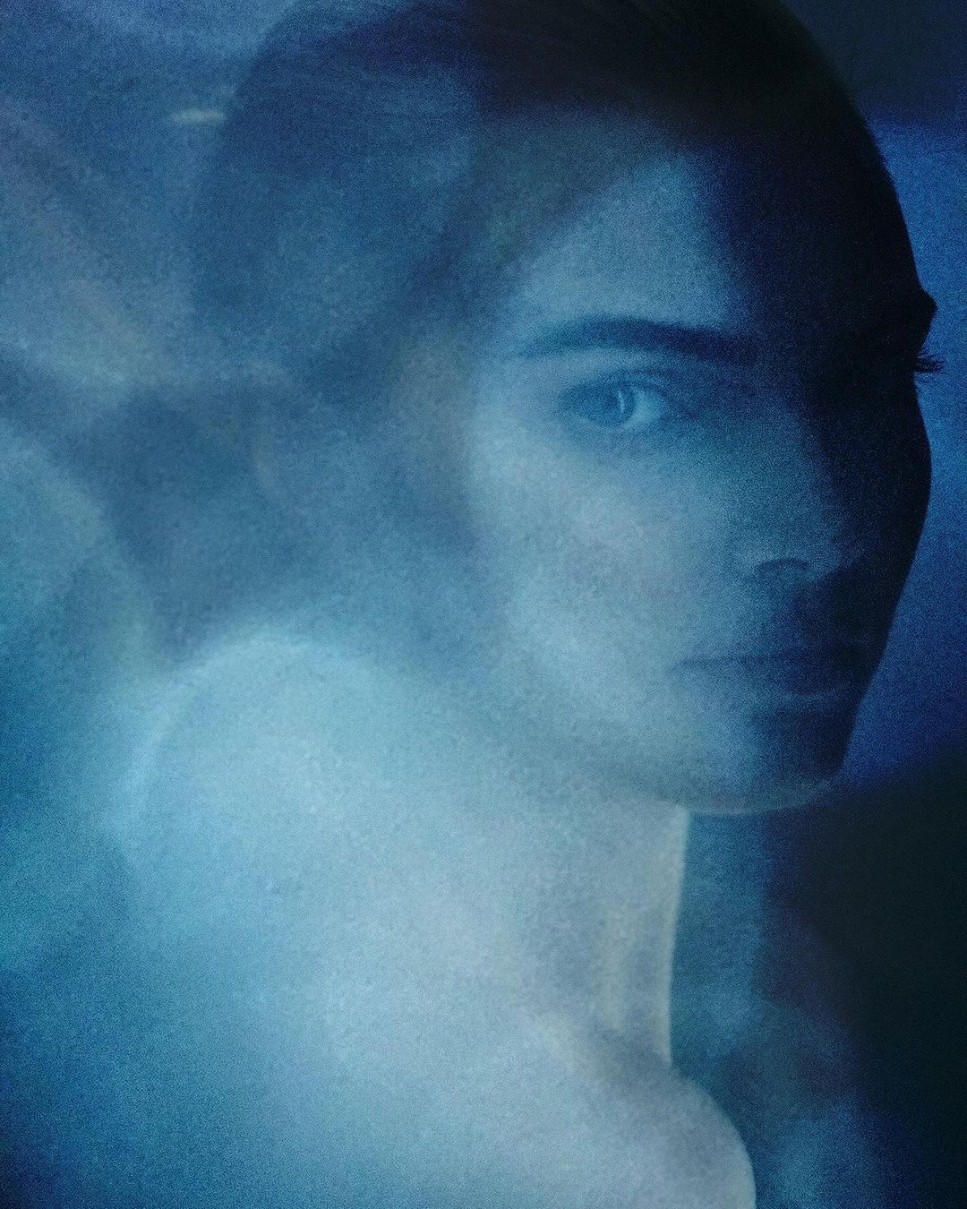 Close-up shot of an adult woman with neutral facial expression in an indoor setting with diffused lighting and a blue color grade.
