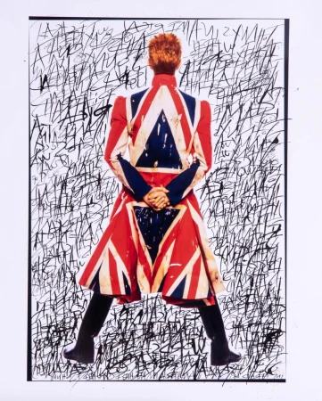 David Bowie, from behind, wears a jacket printed with the British Union Jack flag, against a backdrop of black scribbled text.