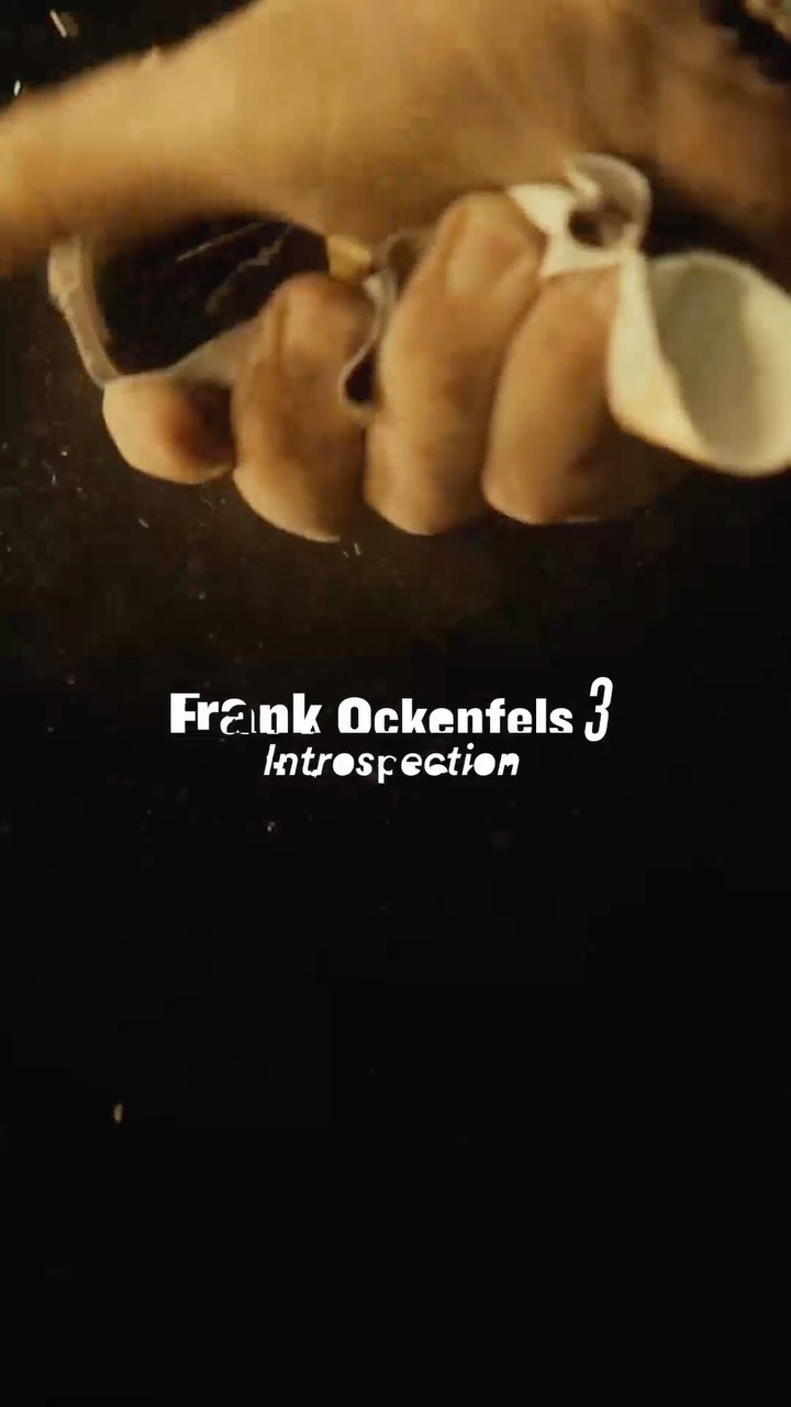 Close-up of a hand gripping white material, with the text overlay "Frank Ockenfels 3 Introspection" on a dark background.