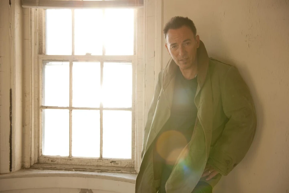 Portrait of a male adult wearing a jacket, posing in front of a window in an interior location, with natural light.