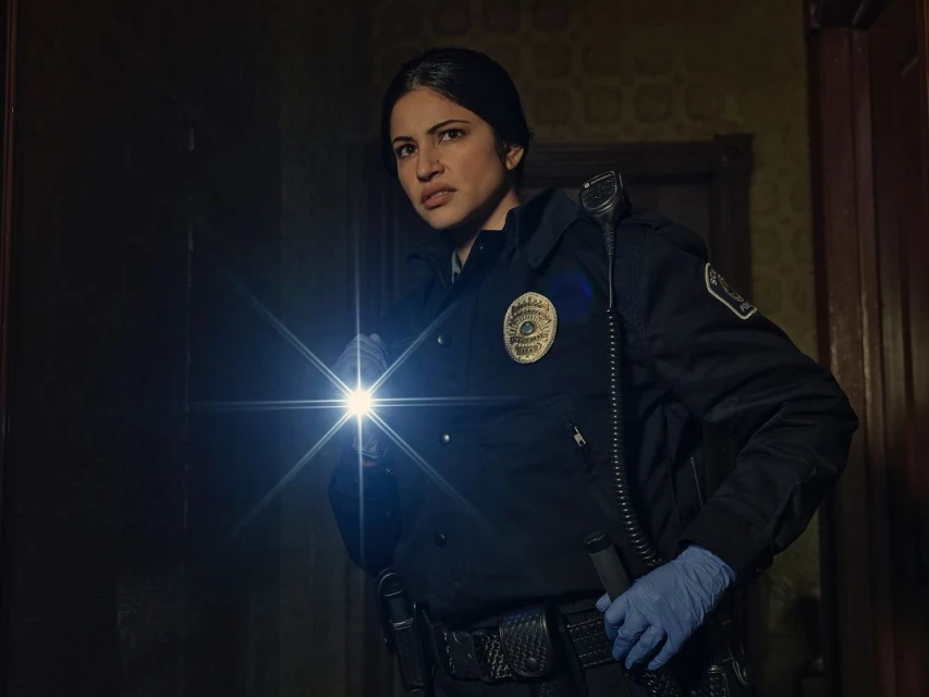 Woman in police uniform shines flashlight in dark room. Focused female officer, wearing blue gloves, with police badge on uniform.