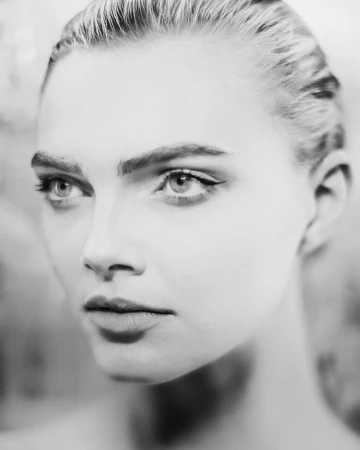 Close-up black and white portrait of a woman with slicked-back hair, winged eyeliner, and a serious expression.