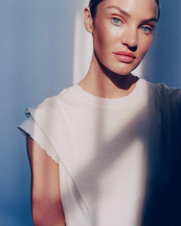 Portrait of a woman wearing a white top with glitter tears under her eyes, captured with dramatic harsh lighting.