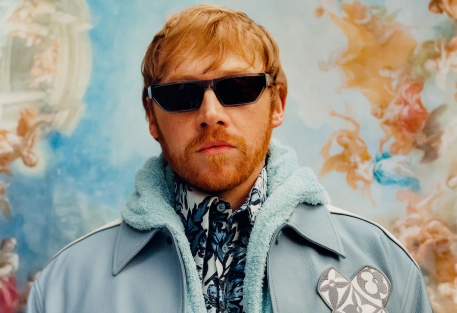 Portrait of red-haired adult male wearing sunglasses, blue jacket with light blue fur-lined hood and floral patterned shirt. 