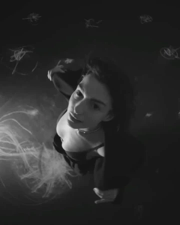Portrait of an adult woman with dark hair looking up in a black and white image with dark clothing and abstract lighting effects.
