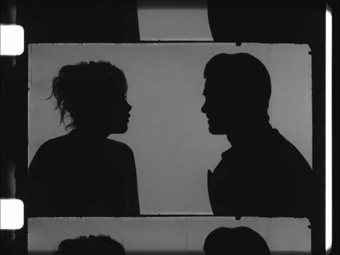Silhouetted profiles of an adult male and female facing each other within a film frame, rendered in black and white.
