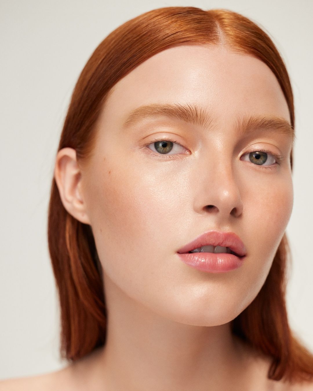 Close-up portrait of a woman with fair skin and red hair against a neutral background, showcasing beauty and natural makeup.