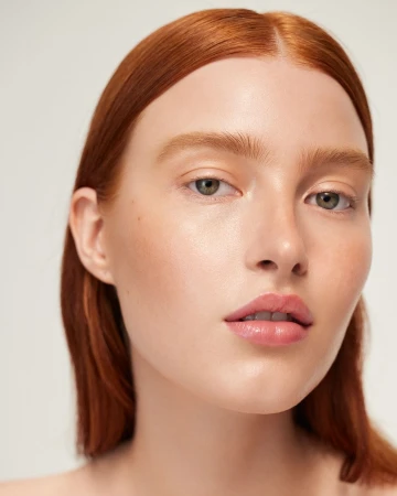 Close-up portrait of a woman with fair skin and red hair against a neutral background, showcasing beauty and natural makeup.