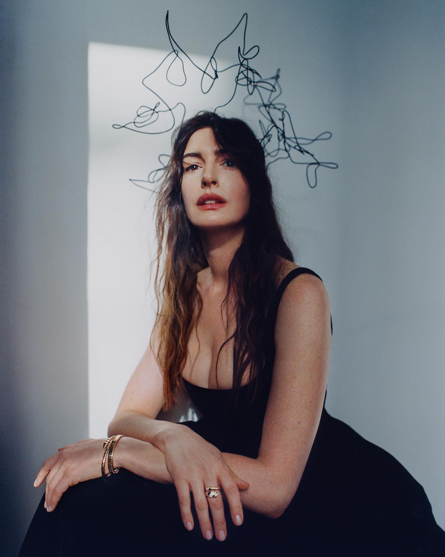 Woman in black dress poses indoors with abstract headpiece. Portrait features jewelry, indoor lighting, and fair skin tones.