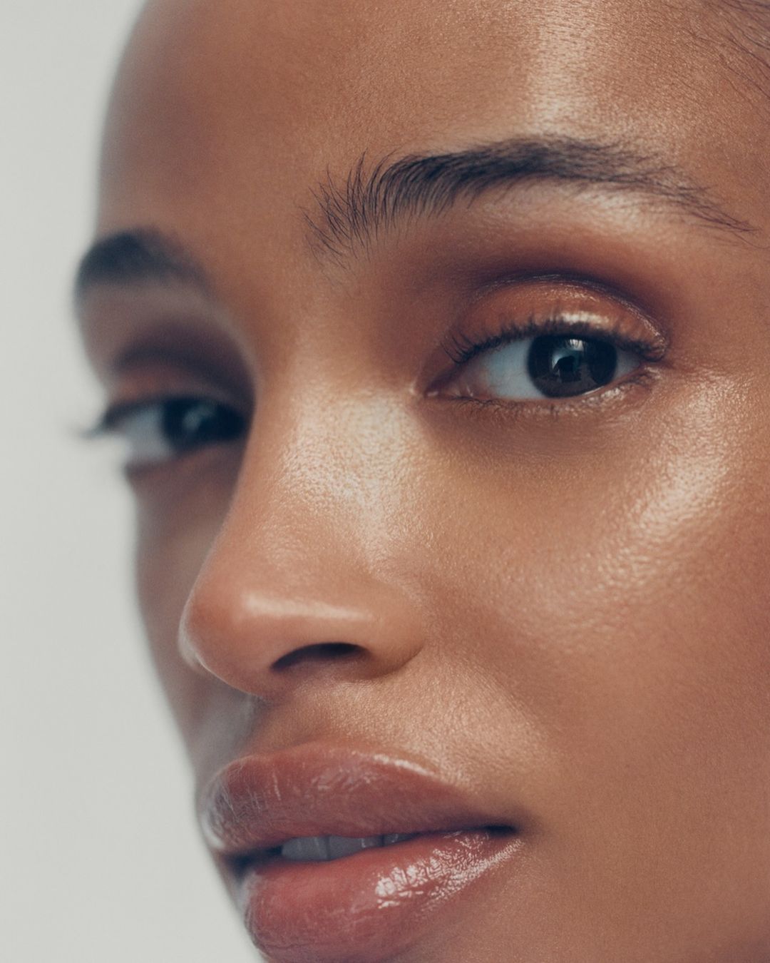 Close-up of a young adult female model with light-brown skin, glossy lips, and natural makeup in a beauty or fashion context.