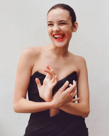 Young woman in a black strapless top with smudged red lipstick laughing against a plain white background