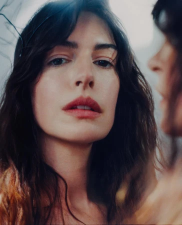 Close-up portrait of a woman with dark wavy hair and rosy lips, captured in a mirror reflection by Heather Hazzan.