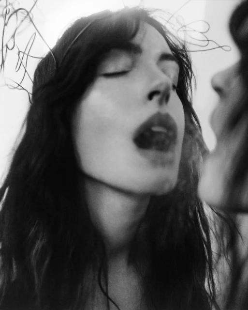 Black and white portrait of a woman with closed eyes exhaling smoke, face reflected in a mirror, with sparse line art around her head.