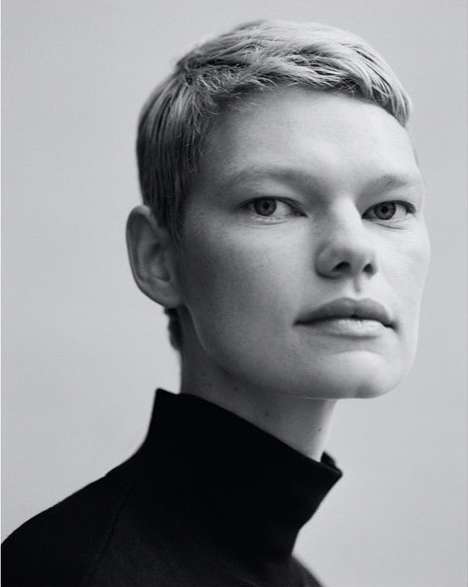 Monochrome portrait of a white adult female with short blonde hair wearing a black turtleneck against a light grey backdrop.