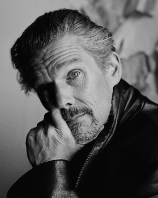 Black and white portrait of a mature man with graying hair, wearing a leather jacket and resting his chin on his hand.