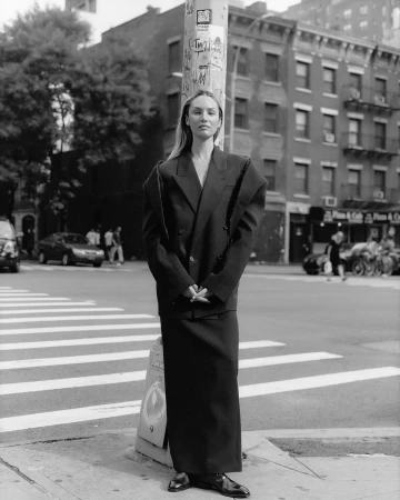 Monochrome portrait of a woman in an oversized dark suit standing on a city street corner by Heather Hazzan