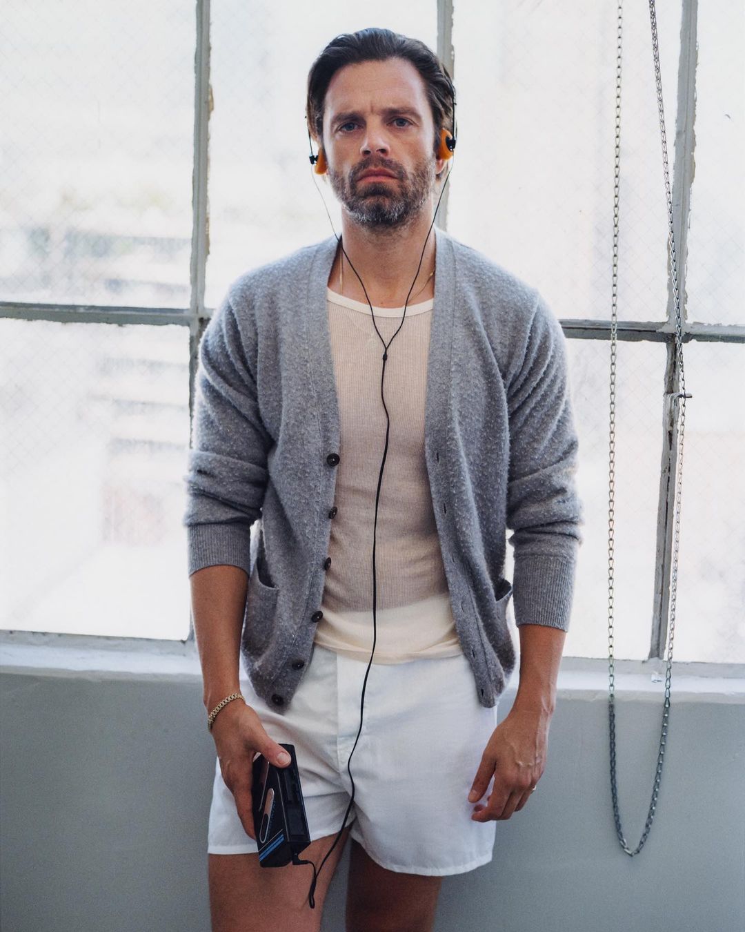 Portrait of an adult man with a beard wearing headphones and holding a Walkman-style cassette player in front of a window in daylight.