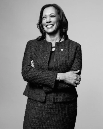 Portrait of Kamala Harris smiling with arms crossed, wearing a textured tweed jacket and skirt against a seamless grey background.