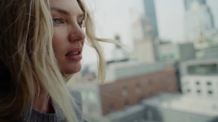 Close-up portrait of a blonde woman with blue eyes outdoors against an urban rooftop backdrop