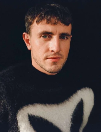Portrait of actor Paul Mescal wearing a black and white patterned sweater against a dark background