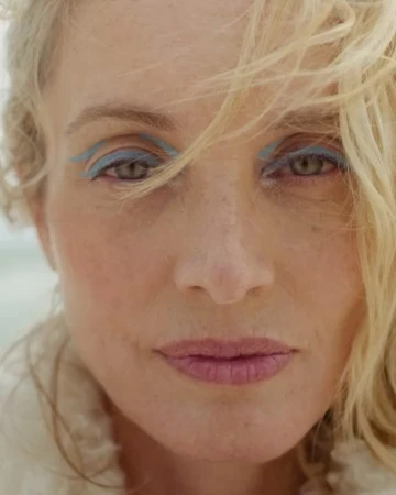 Close-up portrait of a woman with blonde hair, freckles, and light blue eye makeup by Heather Hazzan