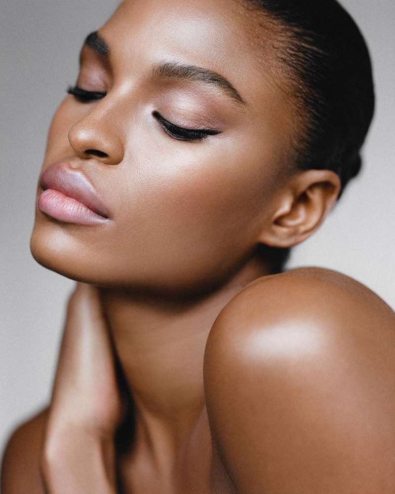 Close-up studio shot of a beautiful adult woman with brown skin, eyes closed, and wearing makeup for beauty and skincare advertisement.