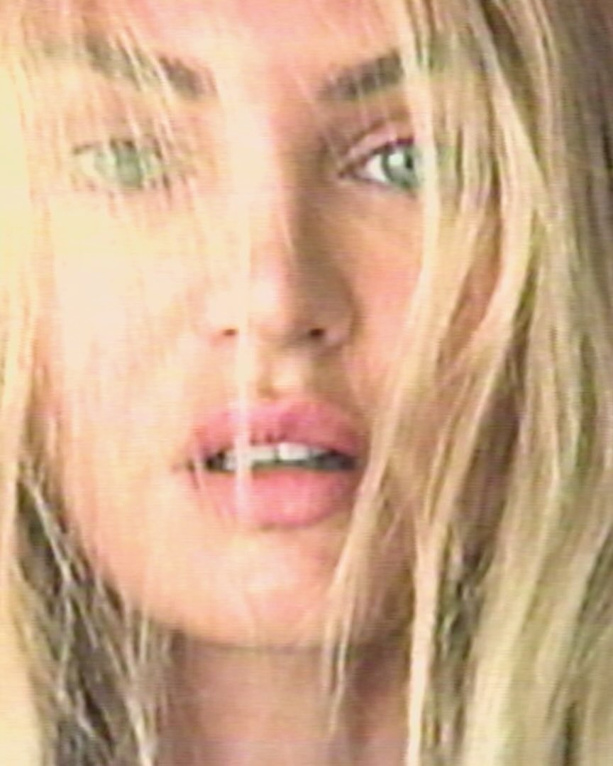 Close-up portrait of a blonde woman with green eyes. The image has a soft, diffused quality with dominant light yellow hues.