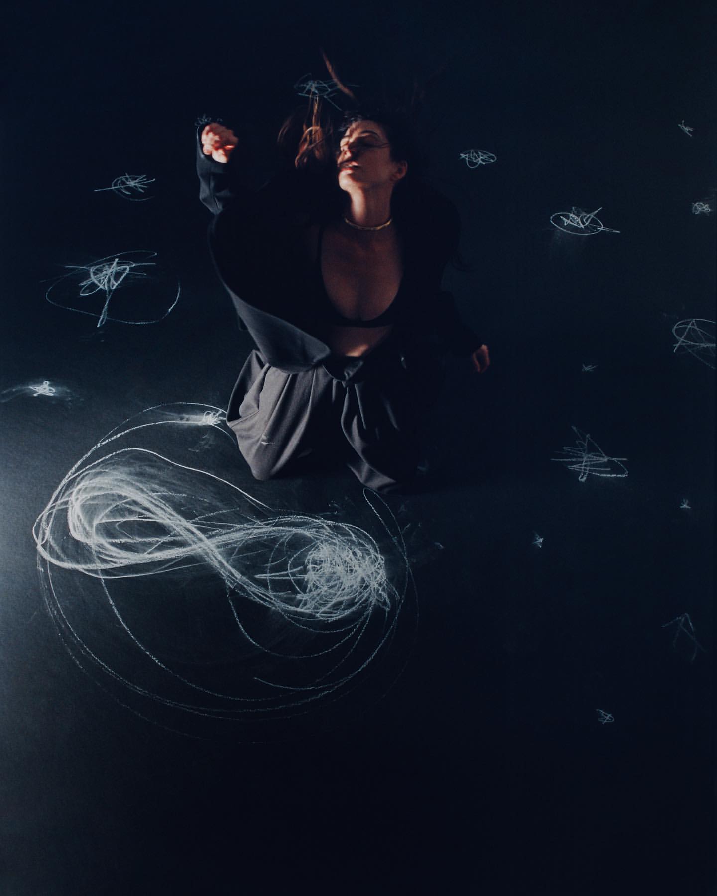 Woman in a black jacket poses with a necklace on a black background with scribbled chalk, creating an artistic and high-contrast portrait.