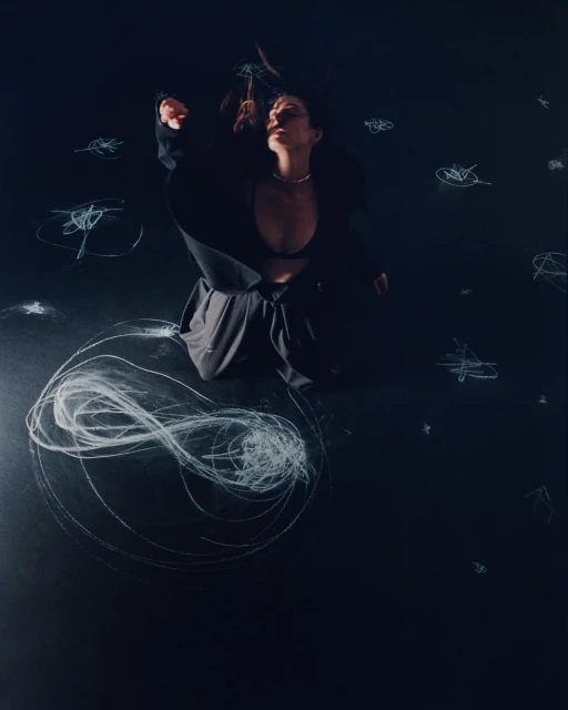 Woman in a black jacket poses with a necklace on a black background with scribbled chalk, creating an artistic and high-contrast portrait.