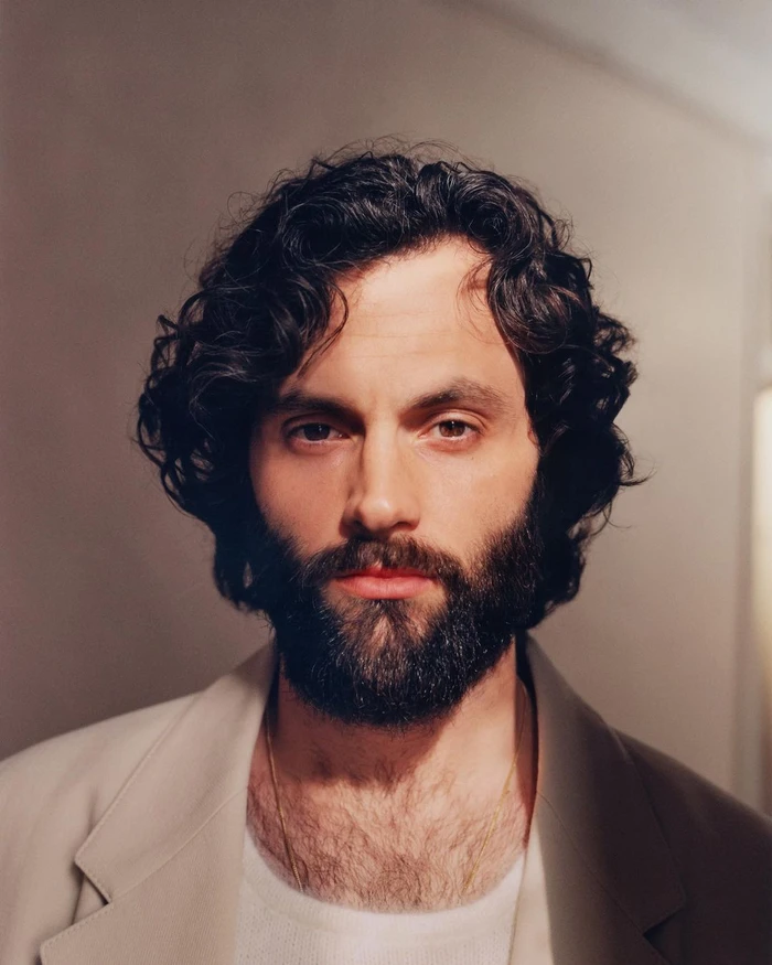 Close-up portrait of Penn Badgley with dark curly hair and beard, wearing a light suit jacket photographed by Heather Hazzan.