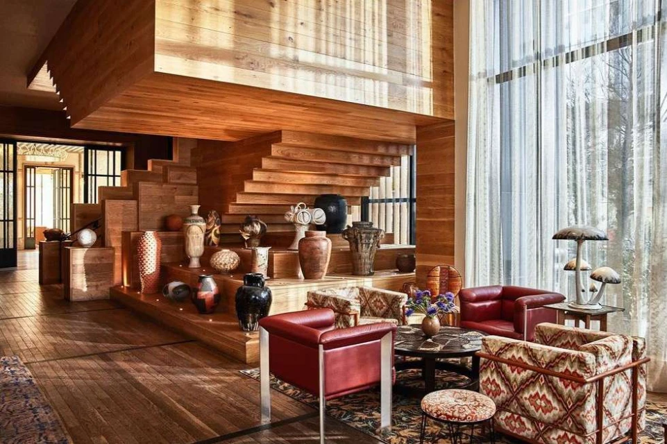 Eclectic home interior featuring warm wood architecture, vases, mushroom lamps, patterned chairs, and a red leather armchair by a window.