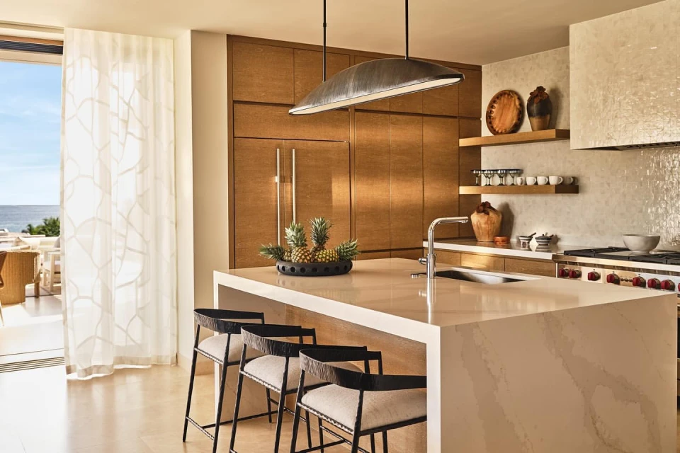 Bright and airy home kitchen featuring a white countertop island with modern black bar stools, hardwood cabinets, and ocean views.